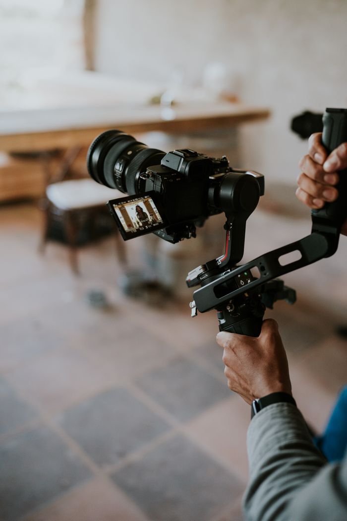 services-03 Close-up of hands operating a DSLR camera mounted on a stabilizer rig in an indoor setting.